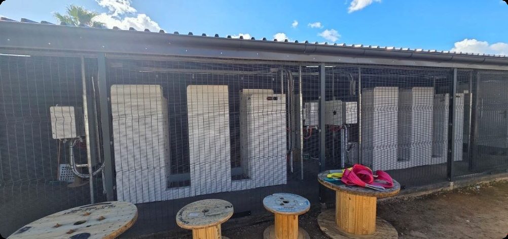 Plant room with inverters and battery cabinets under cover behind secure mesh
